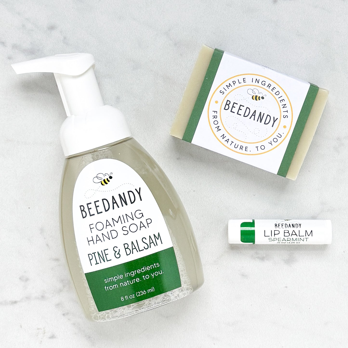 Beedandy Pine & Balsam foaming hand soap bottle displayed with a bar soap and a spearmint lip balm on a light background.