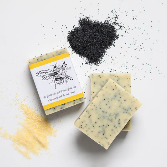 Handmade soap bars with poppy seeds on a white background, including one wrapped bar and two unwrapped bars.