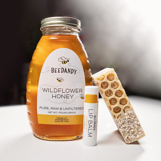 A gift set containing a jar of wildflower honey, a bar of honey oat soap, and a tube of honey lip balm, all branded with 'BEEDANDY'. The items are arranged in front of a white background.