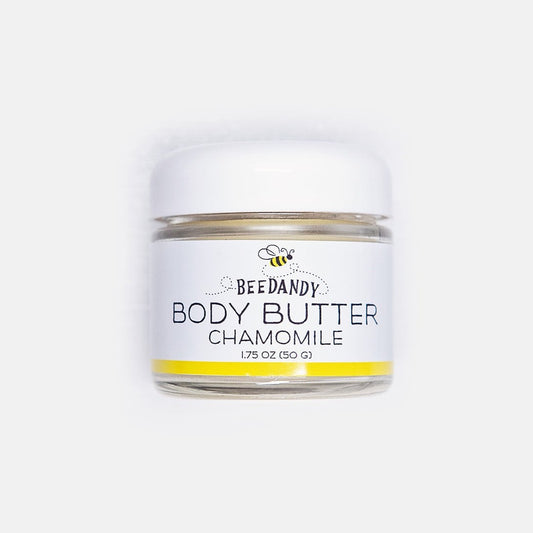 Beedandy chamomile body butter in a small clear glass jar with a white lid, featuring a white label with a bee illustration and yellow accent stripe. All against a white background.