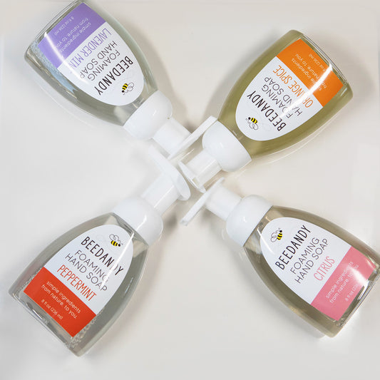 Four pump bottles of Beedandy foaming hand soap in different scents, arranged in circle against white background.