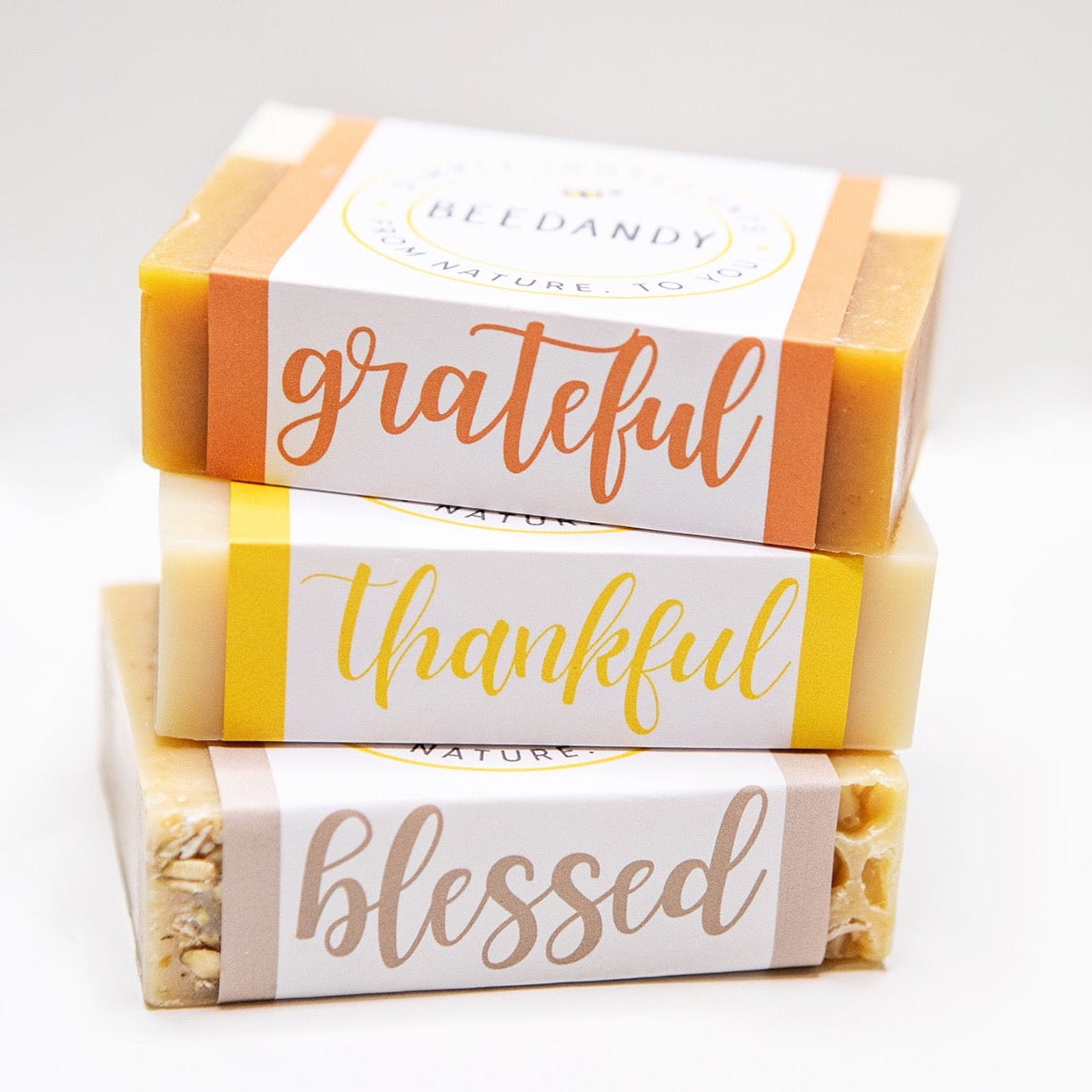 Three bar soaps stacked on top of each other and labeled 'grateful', 'thankful', and 'blessed'. All against a white background.
