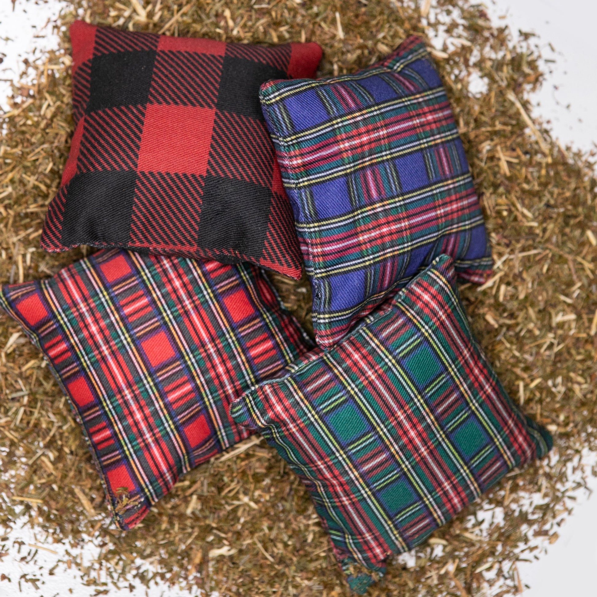 A group of 4 fabric pillows with various plaid patterns, on a bed of balsam fir needles.