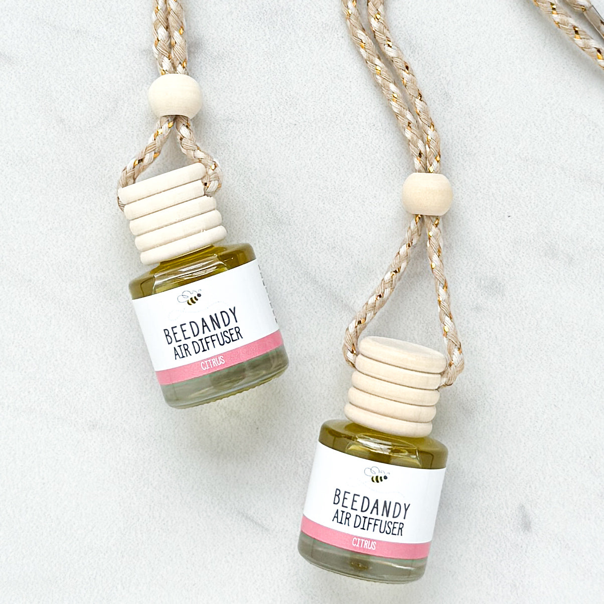 2 glass air diffusers with wooden lids, attached to braided ropes, labeled with white and pink label "Citrus"