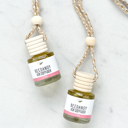 2 glass air diffusers with wooden lids, attached to braided ropes, labeled with white and pink label "Citrus"