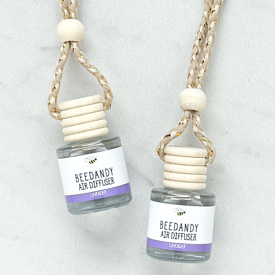 2 glass air diffusers with wooden lids, attached to braided ropes, labeled with white and purple label "Lavender"