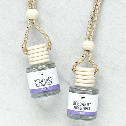 2 glass air diffusers with wooden lids, attached to braided ropes, labeled with white and purple label "Lavender"