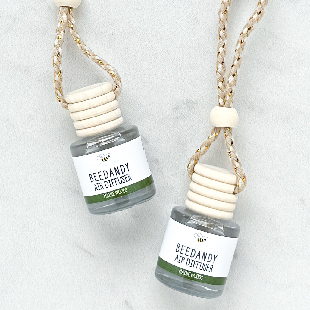 2 glass air diffusers with wooden lids, attached to braided ropes, labeled with white and green label "Maine Woods"