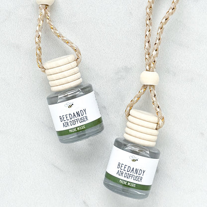 2 glass air diffusers with wooden lids, attached to braided ropes, labeled with white and green label "Maine Woods"