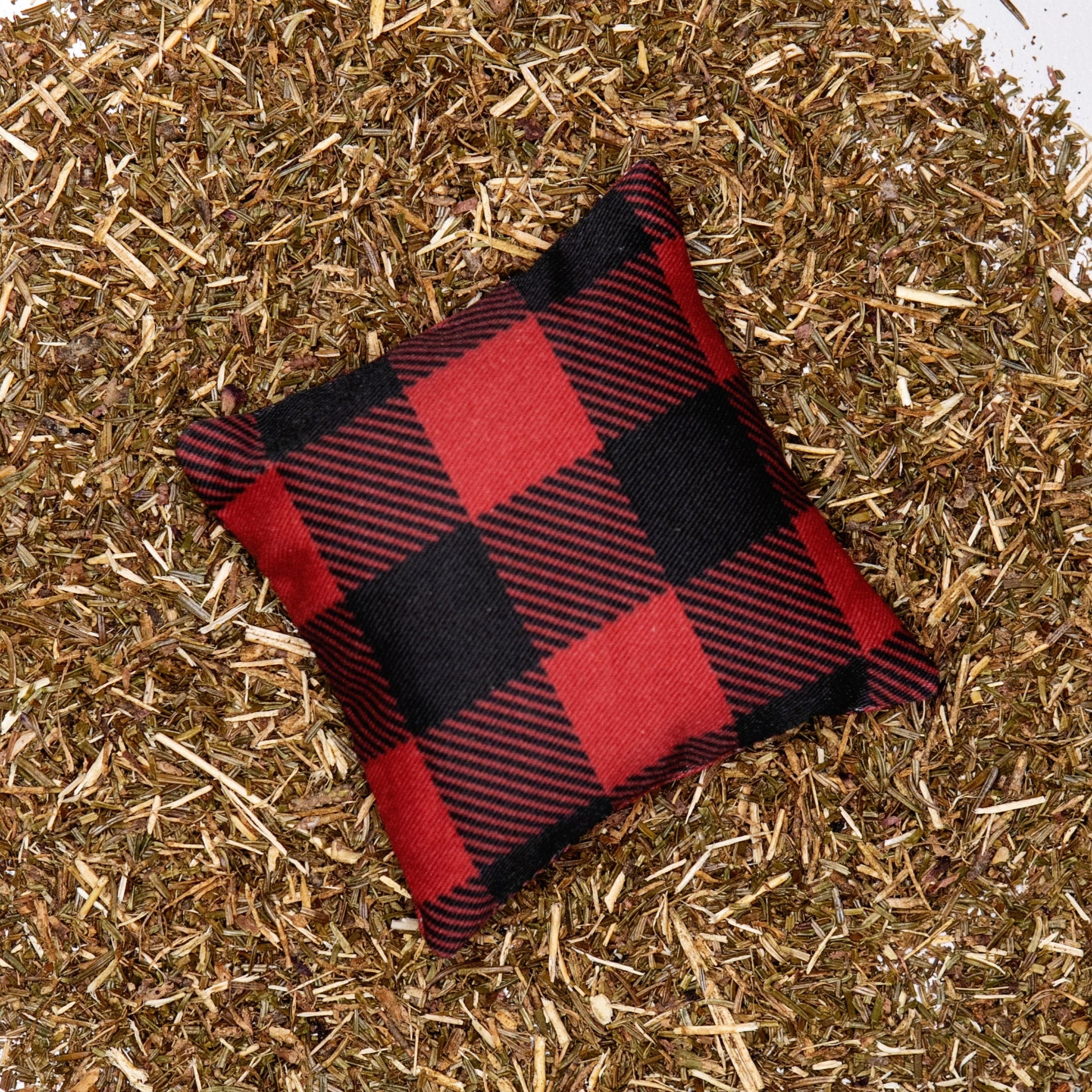 A red buffalo plaid fabric pillow on a bed of balsam fir needles