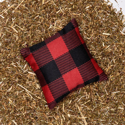 A red buffalo plaid fabric pillow on a bed of balsam fir needles