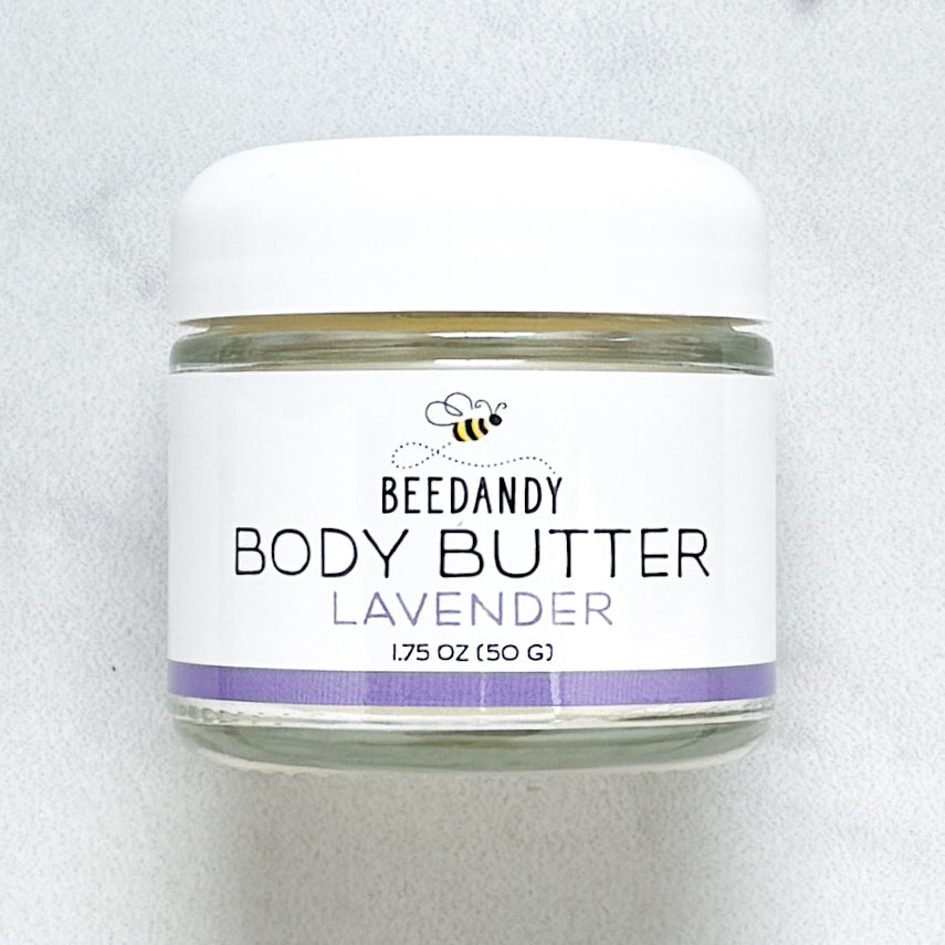 Beedandy Lavender Body Butter in a small clear glass jar with a white lid, shown on a light gray background. The label features a bee logo and reads “Body Butter, Lavender, 1.75 oz (50 g),” with a purple accent band at the bottom.