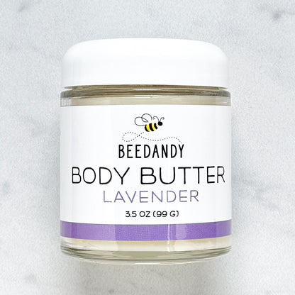 Beedandy Lavender Body Butter in a small clear glass jar with a white lid, shown on a light gray background. The label features a bee logo and reads “Body Butter, Lavender, 3.5 oz (99 g),” with a purple accent band at the bottom.