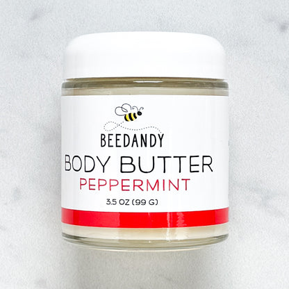 Beedandy Peppermint Body Butter in a small clear glass jar with a white lid, shown on a light gray background. The label features a bee logo and reads “Body Butter, Peppermint, 3.5 oz (99 g),” with a red accent band at the bottom.