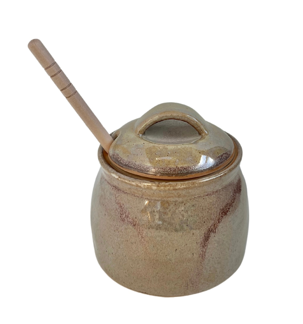 tan honey pot with wooden dipper sticking out top against white background