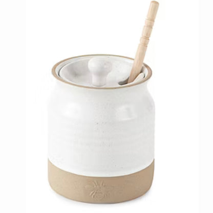 white honey pot with wooden dipper sticking out top against white background