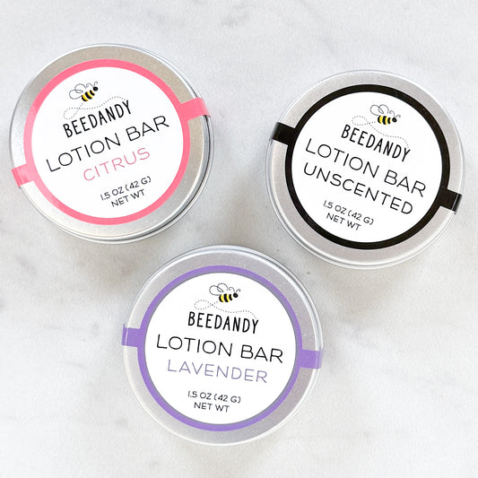 Three metal tins of BEEDANDY lotion bars with labels for citrus, unscented, and lavender on a white background.