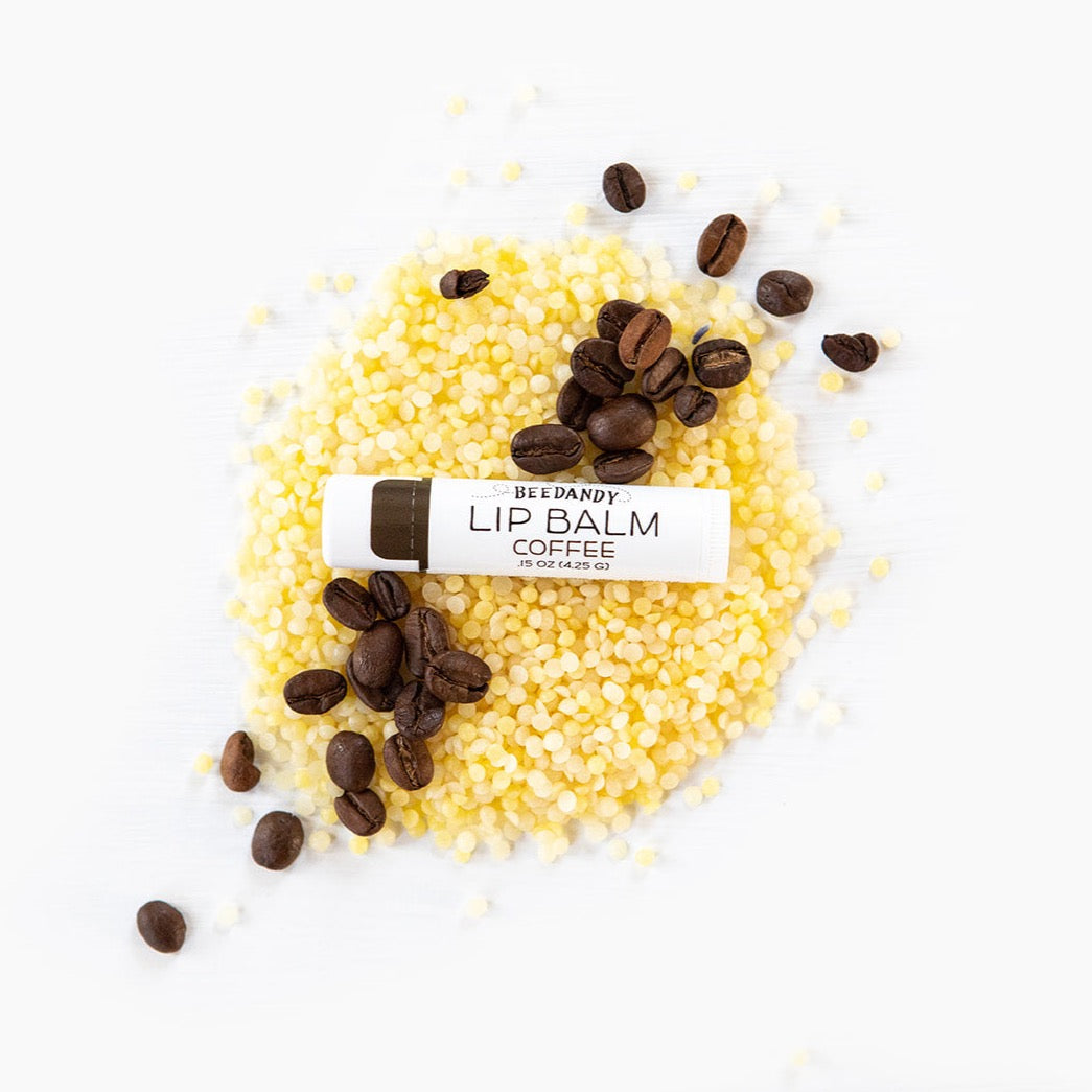 Beedandy coffee lip balm resting on yellow beeswax pellets with scattered coffee beans.