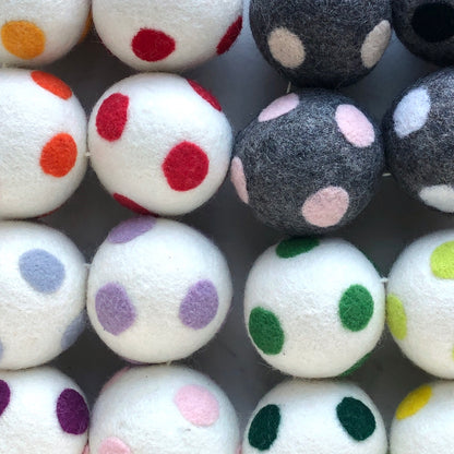 A group of wool dryer balls, some white, some grey, with various colored dots on them.