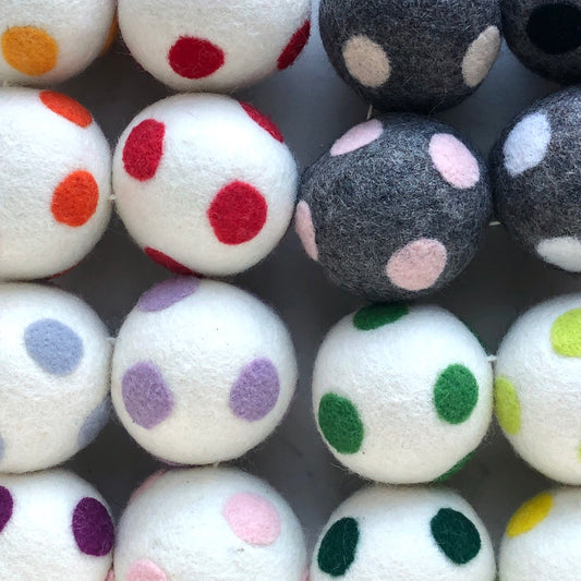 A group of wool dryer balls, some white, some grey, with various colored dots on them.