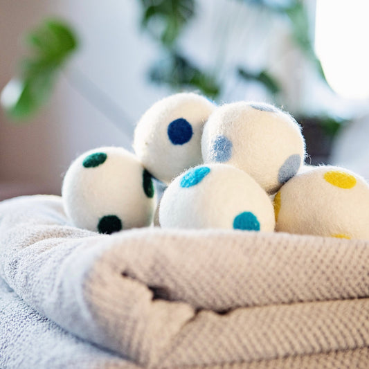 A group of wool dryer balls with blue, green, and yellow felt dots stacked on a folded towel.