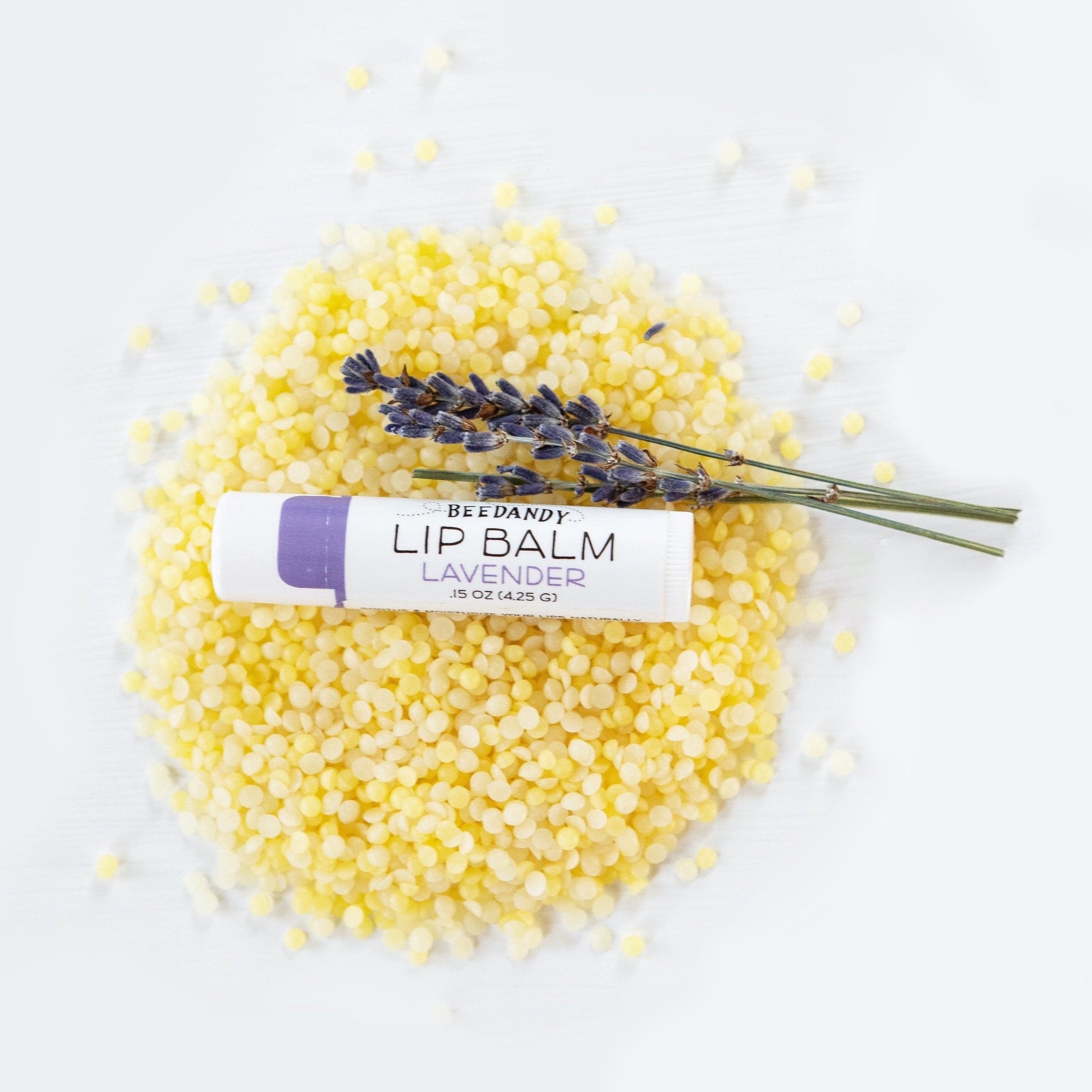 Beedandy lavender lip balm resting on yellow beeswax pellets with sprig of lavender flowers